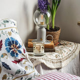 Hygge Daisy and Lavender botanical candle in a cosy cottagecore  style bedroom with fresh  flowers, a lamp arts and crafts style bedding. 