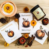Three greetings cards for different occasions featuring a pen and wash orange pumpkin printed on premium quality white watercolour card stock. The cards are lying flat on a wooden surface surrounded by autumnal candles, cinnamon sticks, died flowers and pumpkins giving an autumnal feel.  